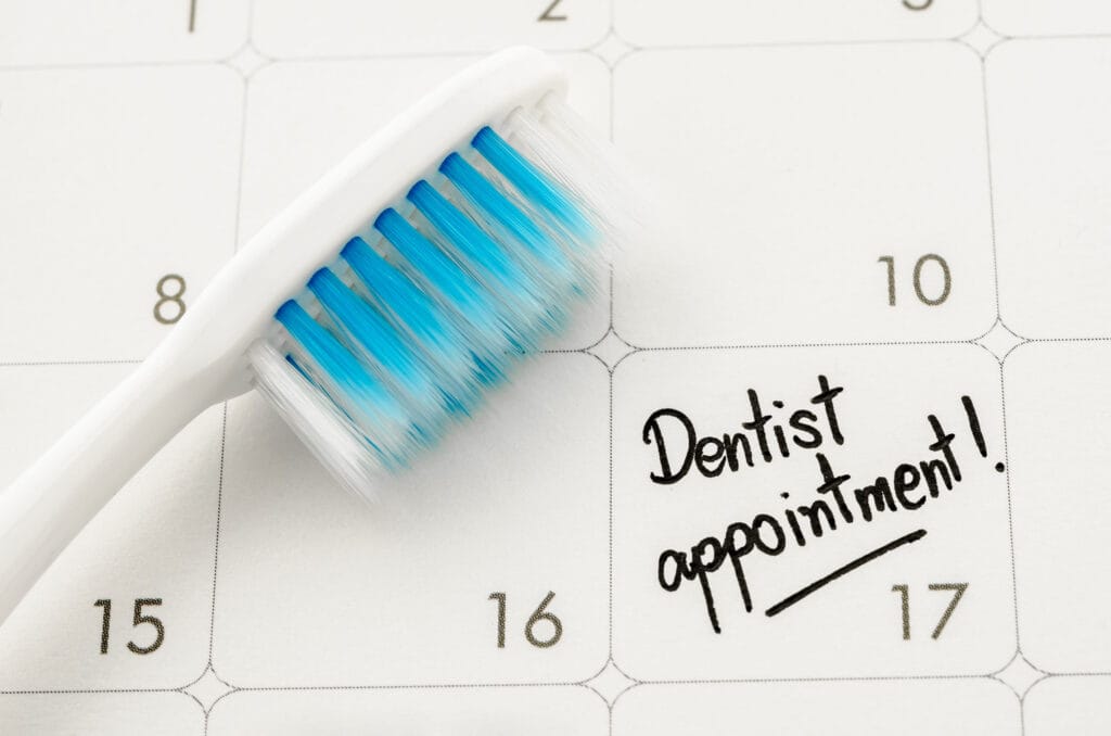 A close-up of a calendar with a white and blue toothbrush resting on it. The date marked is the 17th, with the handwritten note "Dentist appointment!" written in bold black ink.