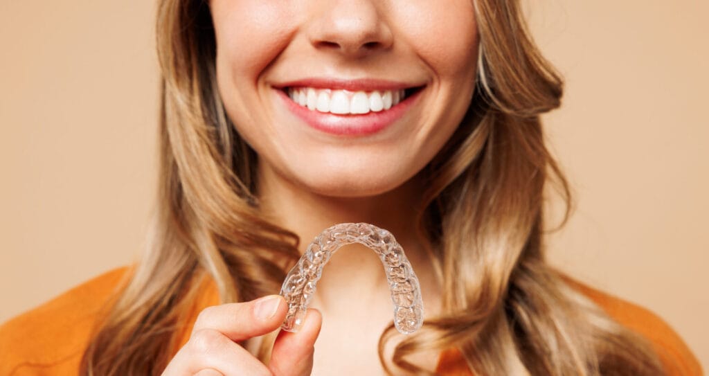 Woman smiling and holding a clear aligner used for Invisalign treatment