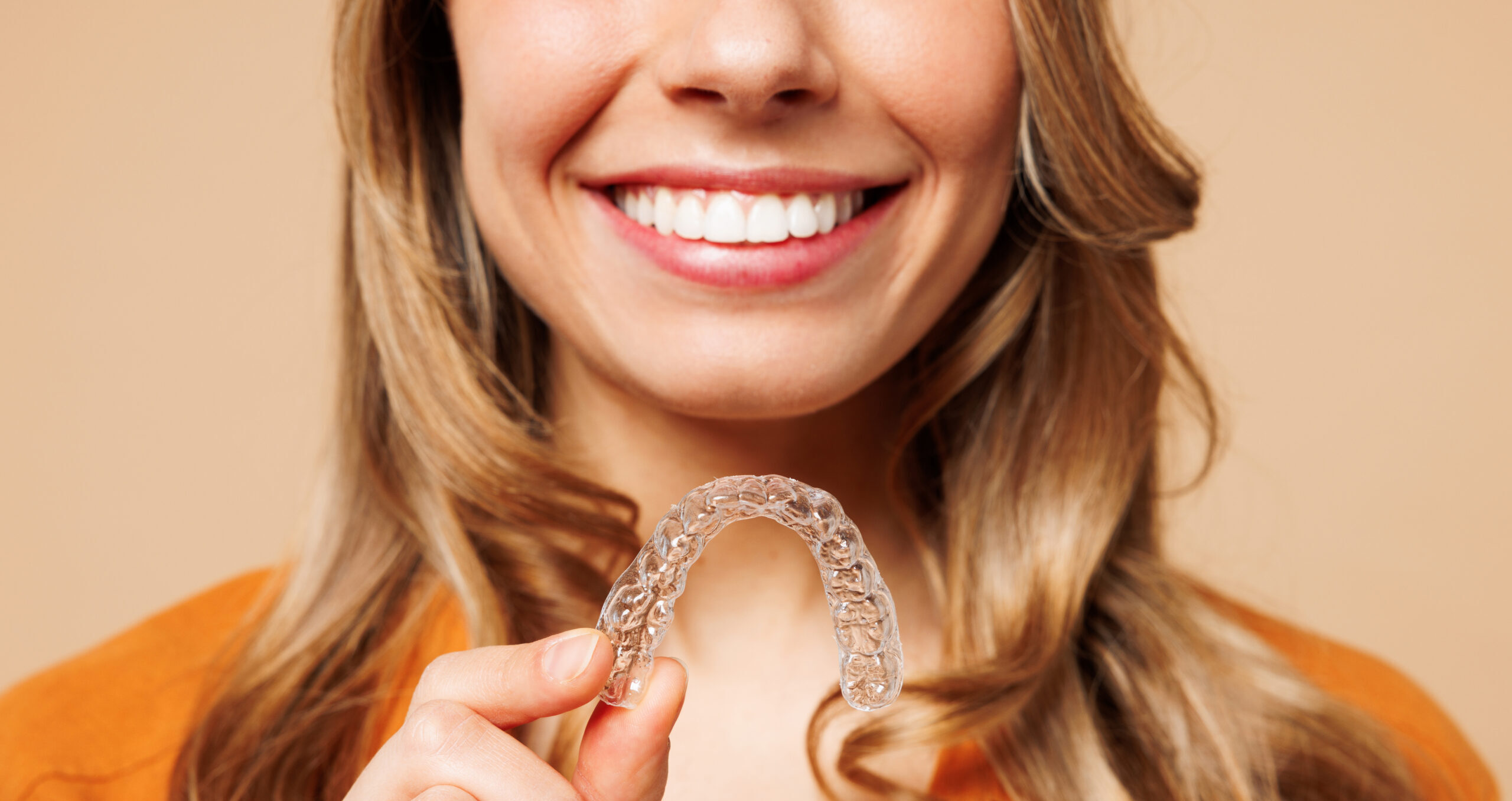 Woman smiling and holding a clear aligner used for Invisalign treatment