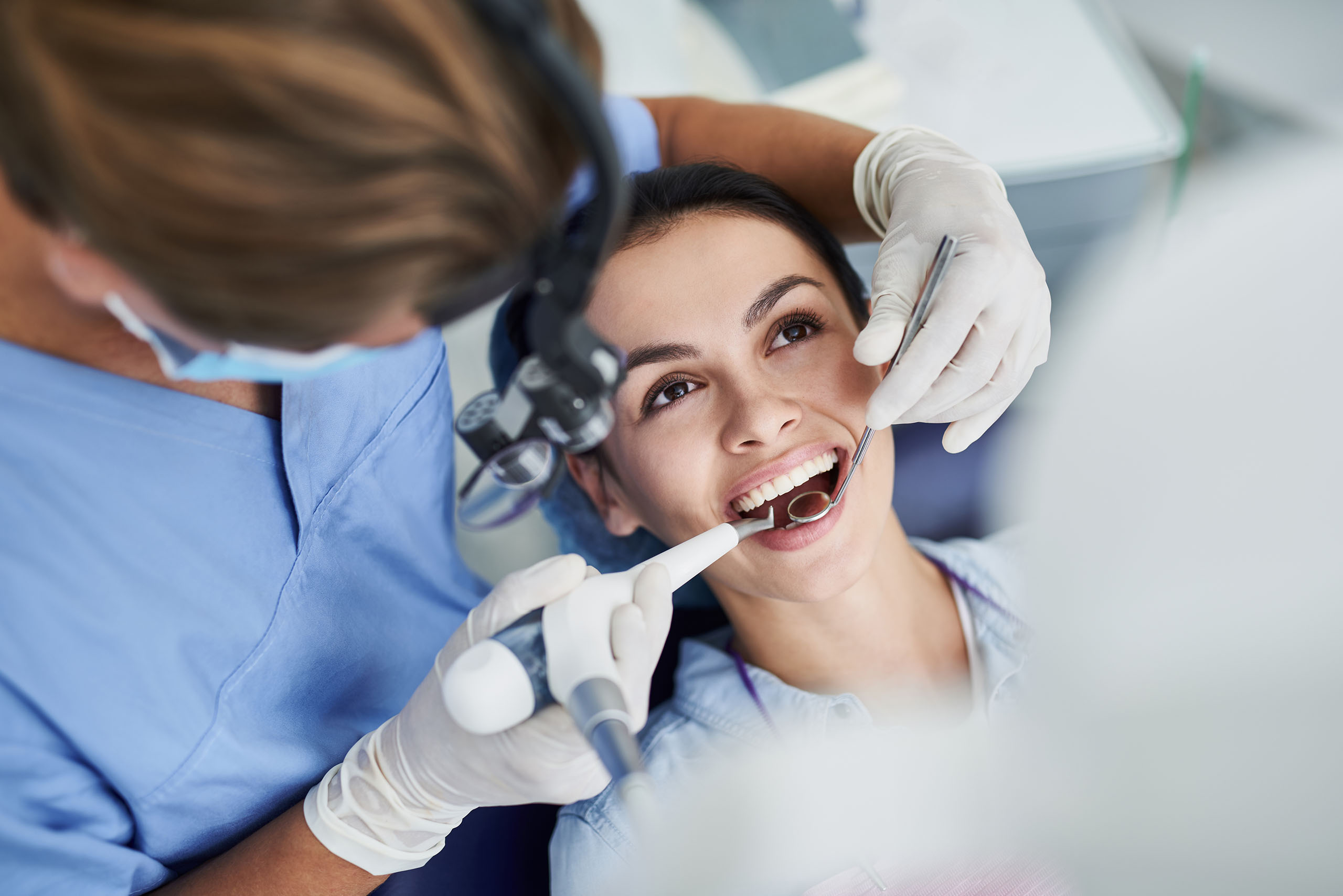 Dentist performing a dental cleaning on a smiling patient in a modern clinic.