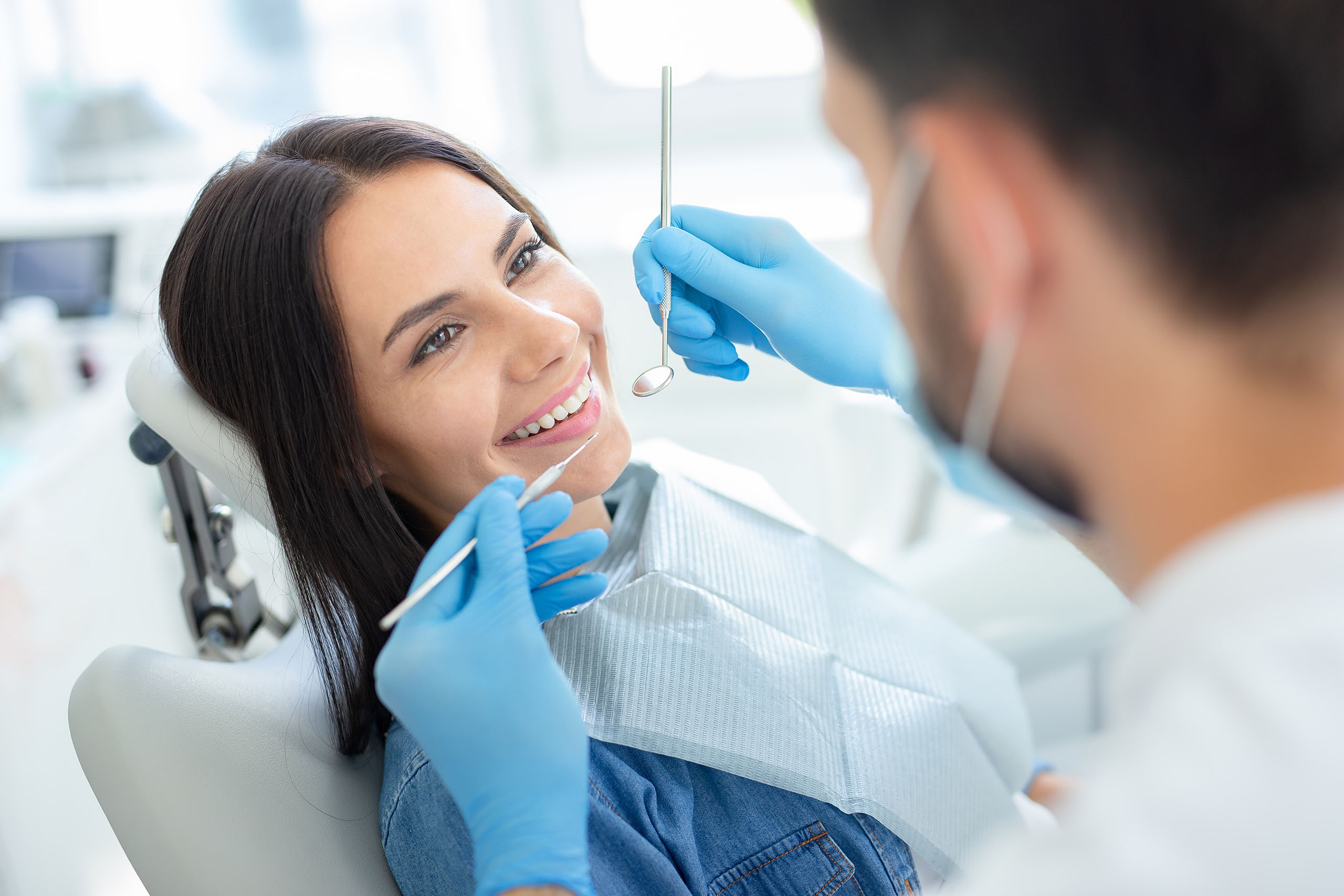 Dentist examining a smiling patient with a dental mirror and probe in a bright, modern clinic.