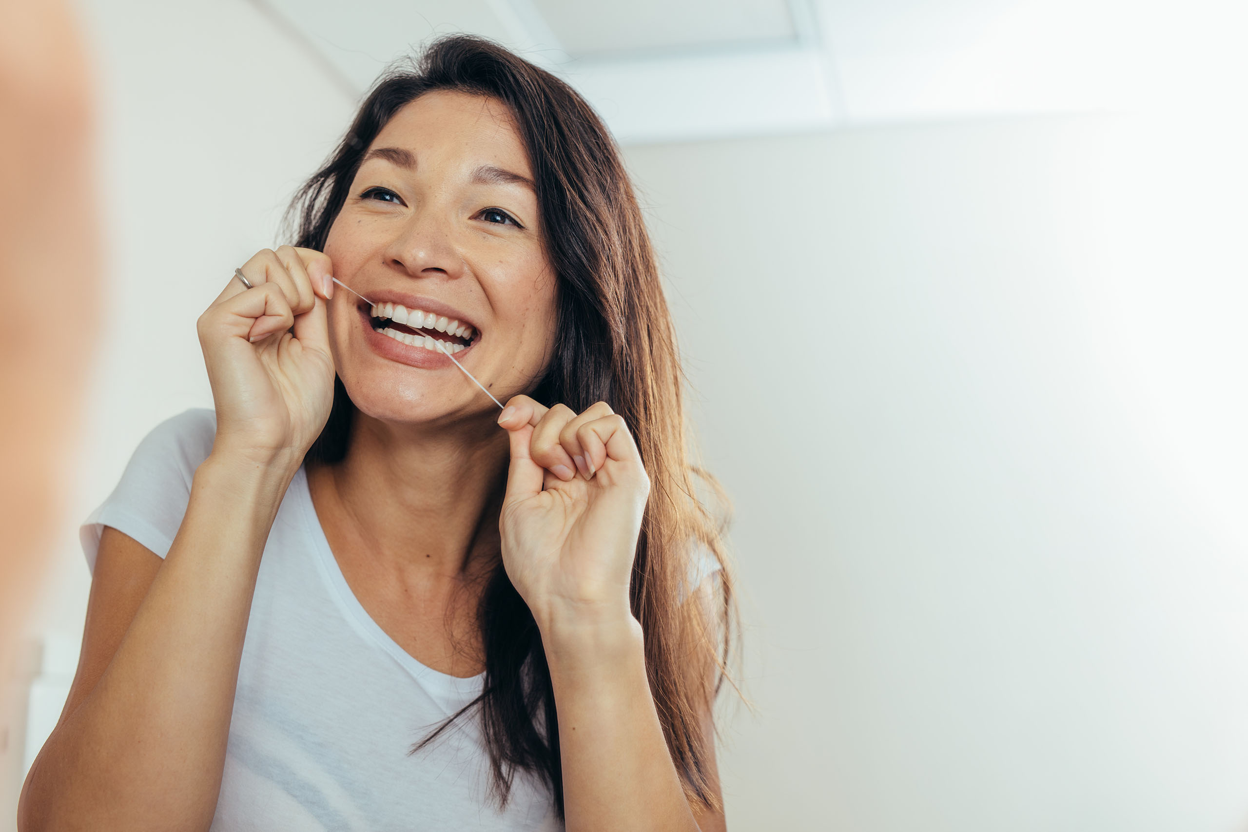 Adult woman flossing her teeth in a bright bathroom, demonstrating proper daily oral hygiene to prevent gum recession.