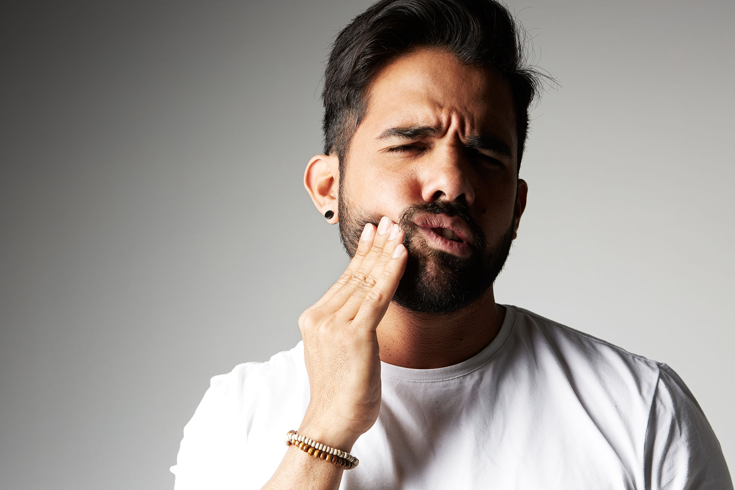 Man touching his cheek with a pained expression, suggesting tooth sensitivity or enamel damage