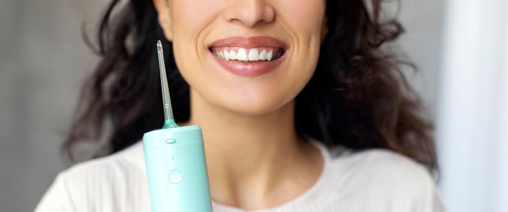 Smiling woman holding a cordless water flosser, highlighting an oral care device for cleaning between teeth