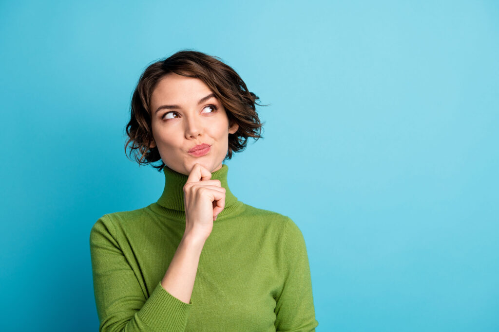 Woman in green turtleneck touching chin and looking up thoughtfully against a blue background, representing decision-making or risk assessment